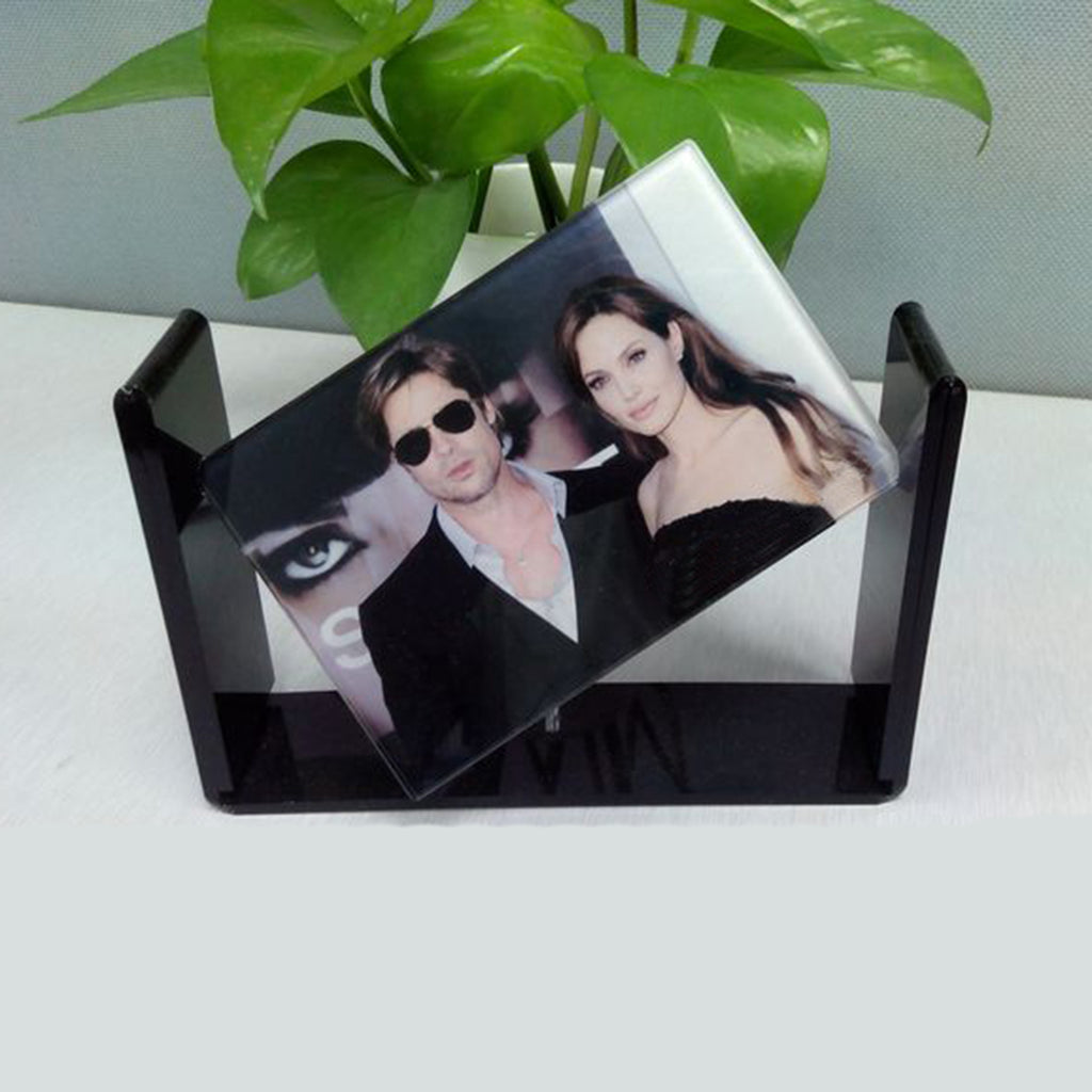 Black photo frame with a printed image of a couple on a white surface with a green plant in the background.